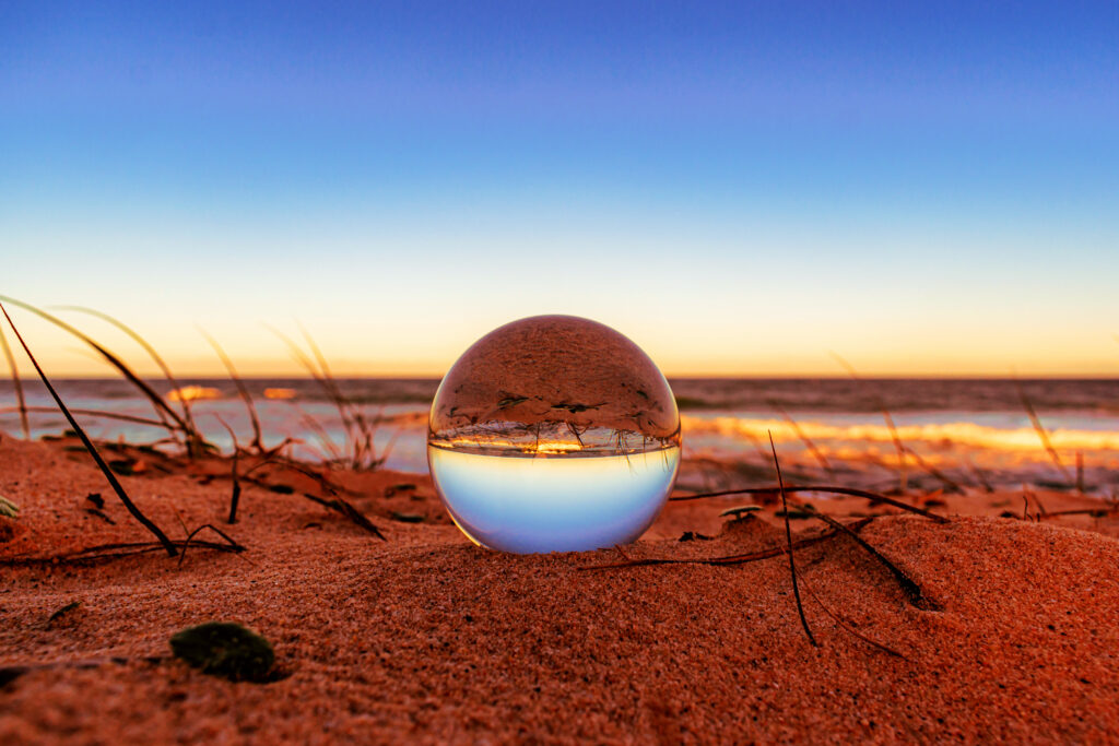 A closeup of a crystal ball on the beach with the surroundings reflecting on it